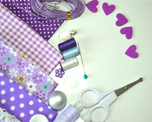 Composition of sewing accessories including white-dotted and floral cotton fabrics in lilac and mauve, scissors, buttons, sewing spools. Scrapbooking and DIY. Hobby and needle work background. 