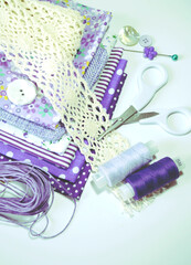 Composition of sewing accessories including white-dotted and floral cotton fabrics in lilac and mauve, scissors, buttons, sewing spools. Scrapbooking and DIY. Hobby and needle work background. 