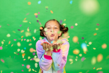 a little girl on a green isolated background in a bright suit blows away a streamer. Space for...