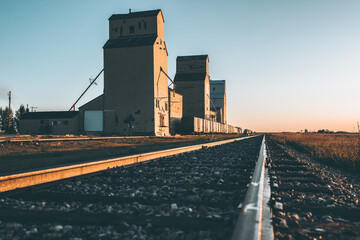 Grain silos and railway tracks running past them at sunrise  - obrazy, fototapety, plakaty