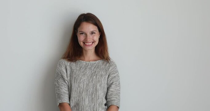 On grey studio background standing in casual sweater young woman having sincere smile feels confident pose alone looking at camera. Millennial generation person, dentistry beauty treatment ad concept