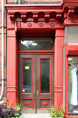 Red vintage shabby-looking entry door in New York decorated with columns and corbels. USA.