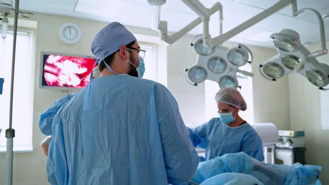 Surgical work in the operating theater. Team of doctors in medical uniform performing an operation and observe the process on the screen of monitors.