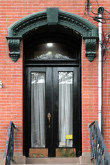 Black vintage shabby-looking entry door in New York decorated with arch and corbels. USA.