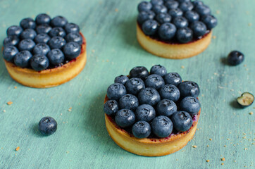 Mini tarts decorated with fresh blueberry on green background