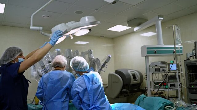 Medical team perform operation. Medical assistant puts the lamp over the doctors before the surgery in operating room.