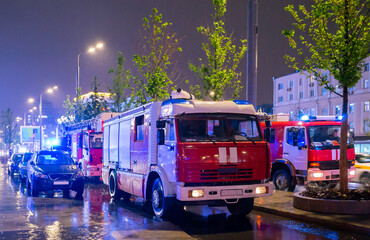 Fototapeta na wymiar Fire engines in the courtyard of the apartment building where the fire occurred, at night during the rain.