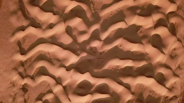 Aerial view of a beige-golden waving pattern of sand dunes at sunset. 4K drone shot of desert nature revealing the climate change concept. Dry heat weather showing the global temperature increase