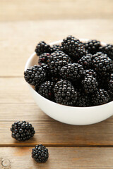 Blackberry fruit in bowl on grey wooden kitchen table.