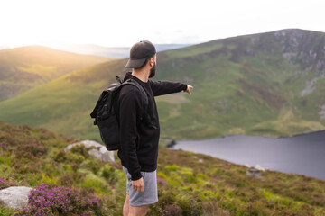 Young man on the mountain pointing to a spot in the landscape, beautiful sunset in the background.