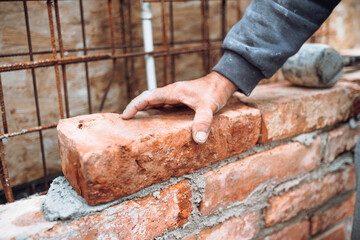 Construction mason,  industry worker laying bricks and building walls on construction site. Detail of hand adjusting and placing bricks