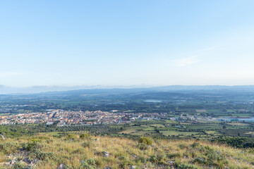 Views from a hill of a village in the middle of fields and the unfocused mountains in the background on a sunny day