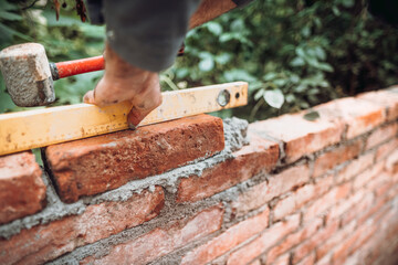 professional construction worker laying bricks and building walls in industrial site. Detail of hand adjusting bricks.