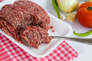 Uncooked minced beef meat,in white package with spoon and vegetables,close up.