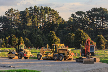 Road-making vehicles in the countryside. From left to right are a road roller, a grader, and a crawler excavator