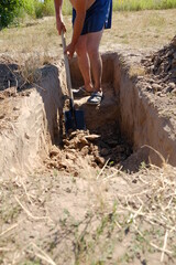 a man in blue shorts digs a deep hole with a shovel. a man digs a grave in a cemetery in the afternoon