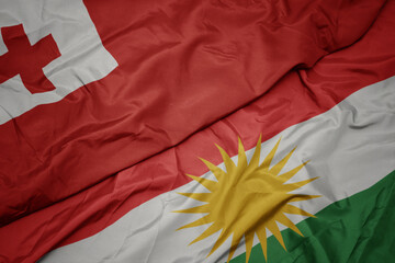 waving colorful flag of kurdistan and national flag of Tonga .
