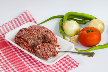 Uncooked minced beef meat,in white package with spoon and vegetables,close up.