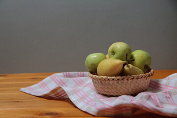 frail of apples and pears on a towel on wooden table against gray background