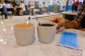 Tea and coffee in restaurant cafe, face mask on white marble table during coronavirus outbreak. blur bacground. New normal dining concept during covid-19, reopening