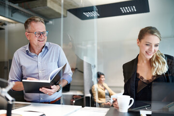 Smiling male and female colleagues working while standing at desk with glass shield in office during coronavirus