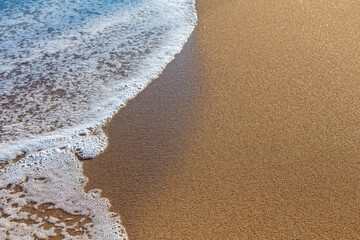 Surf wave on a sea beach. Wet sand and sea foam as a background or texture. There is a place for text.