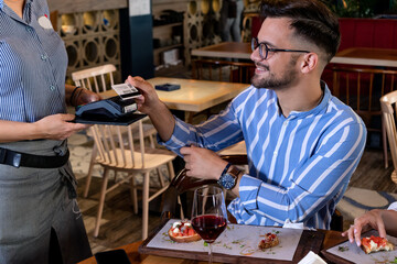 Man paying the bill with his credit card, after dinner with his girlfriend in a modern retro style restaurant. Fine dining and gentleman manners concept.