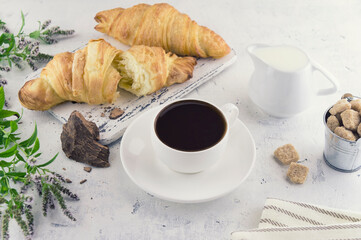 Croissants, a cup of coffee with a slice of natural cocoa liquor, milk and cane organic unrefined sugar on a light vintage provence background. Healthy vegetarian food. Food photo