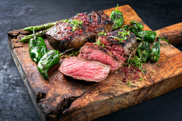 Gegrilltes dry aged Wagyu Roastbeef Steak mit grünen Spargel und Chili angeboten als close-up auf einem alten rustikalen Holz Board