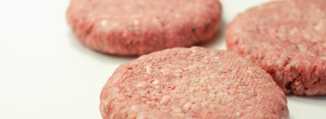 Raw beef burgers with a pinch of salt and black pepper on the white background