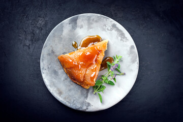 Traditional French tarte tatin with apples and vanilla offered as top view on a modern design plate with rustic background with copy space