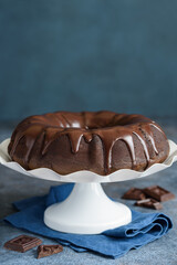Traditional chocolate bandt cake with chocolate icing on a white stand on a blue background. Selective focus. Chocolate pastry.