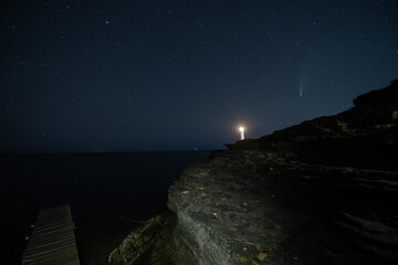 HDR Landscape view of Neowise comet over white Lighthouse at night sky at beach
