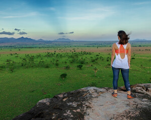 Fototapeta premium Young woman looking into the horizon of the beautiful landscapes of Kidepo Valley National Park, Uganda, Africa. The woman rests on top of a kopje after a nice hike.