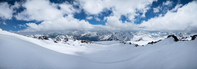 Fototapeta na wymiar alpine panorama of the large Caucasian ridge covered with snow on a sunny day with variable clouds. Ideal slopes for skis and freeride ski and snowboarding