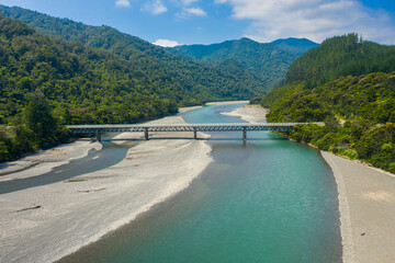 An aerial view of Pacific Coast Highway 35 bridge over the Motu River. Mountains a forest leading off into the background.