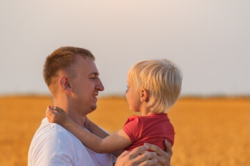 Portrait of dad and child boy on background of yellow fields. Son hugs father