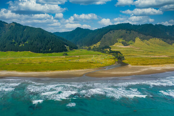 An aerial view of East Cape Campground next to the Pacific Ocean. Located on the eastern tip of the North Island of New Zealand. Mountains a forest leading off into the background.