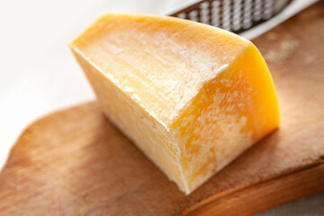 Piece of cheese. Piece of parmesan on a wooden board. Cheese grater.