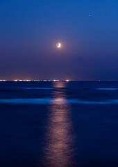 Vertical seascape with seasparkle and a waxing crescent moon in the sky. © sharon
