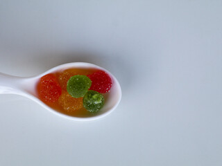 Sweet mixed color jelly candy in a white spoon against white background with copy space