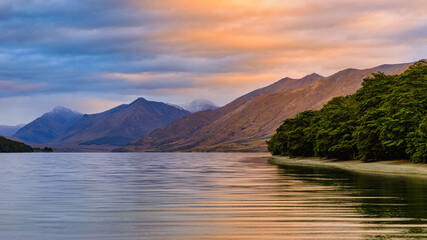 North Mavora Lake surrounded by forests with mountains in the background at sunset on a cloudy day.
