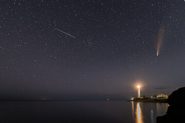 Panoramic HDR Landscape view of Neowise comet over white Lighthouse at night sky