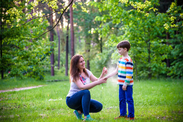 Young woman mother applying insect repellent to her son before forest hike beautiful summer day or...