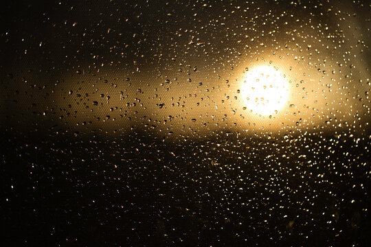 Regentropfen auf der Windschutzscheibe im Auto, dahinter der Sonnenuntergang 