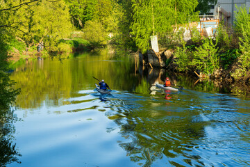 Two people are kayaking along the city river on a sunny day