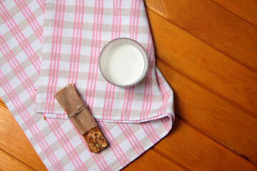 granola bar and a glass of milk on a towel on wooden background flat lay