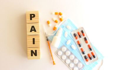 The words PAIN is made of wooden cubes on a white background with medical drugs and medical mask. Medical concept.