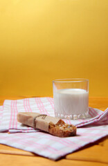 granola bar and a glass of milk on a towel on wooden table against yellow background