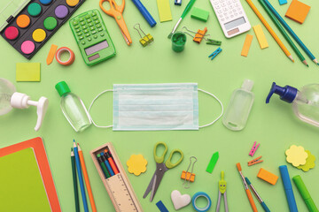 Coronavirus spread prevention measure at school. Surgical mask, alcohol disinfection gel and stationery on green pastel background,